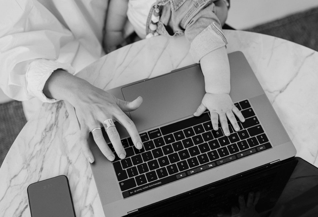 Frauenhand auf der Tastatur eines Laptops und eine Kleinkindhand, die ebenfalls auf der Tastatur des Laptops ist.
