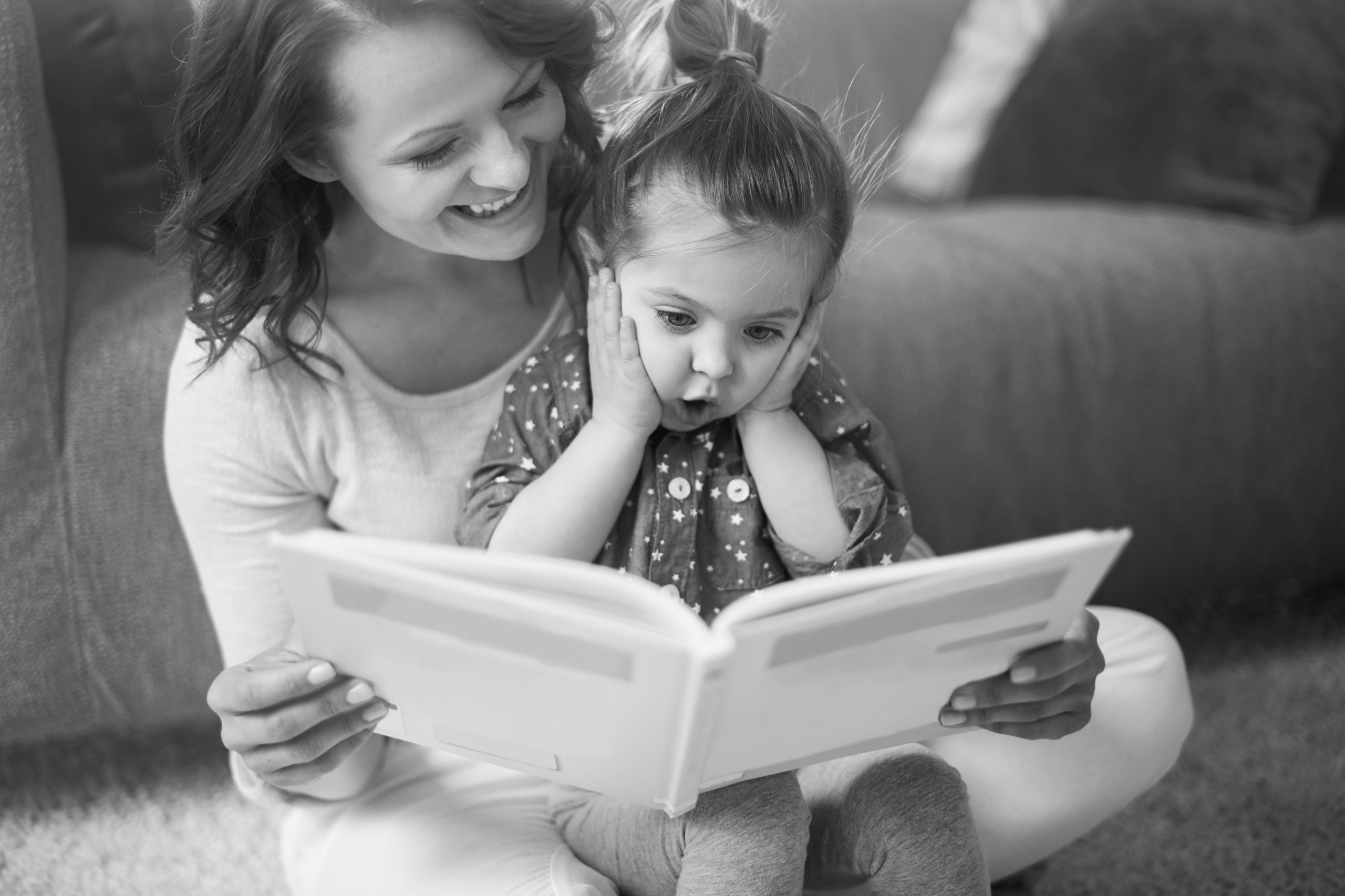 Junge Frau mit einem kleinen Mädchen auf dem Schoß, die gemeinsam ein Buch lesen.